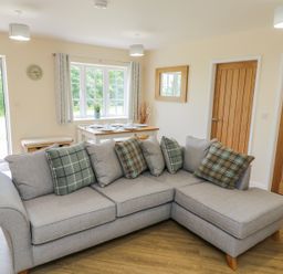 A living room with a grey corner sofa and dining table near a window at Ryedale Country Lodges - Willow Lodge Kirkbymoorside