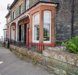 A stone house with red window frames and a red door with black iron railings at Sefton House in Keswick