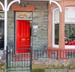 Front entrance of a building with a red door slightly open black gate and window reflecting a red car at Sefton House in Keswick
