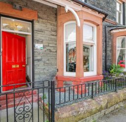 A stone house exterior with a red door black iron gate and bay windows at Sefton House in Keswick