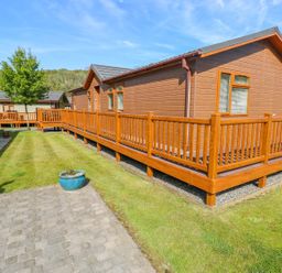 Exterior view of wooden lodges with fenced decks and a grassy area in between at Serendipity - Heritage Park Stepaside near Kilgetty