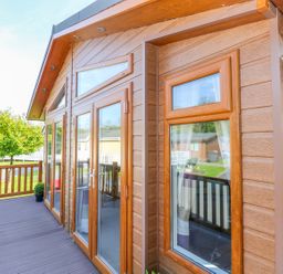 A wooden deck with railing and glass doors attached to a building at Serendipity - Heritage Park Stepaside near Kilgetty
