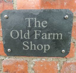 A black stone sign with the text The Old Farm Shop mounted on a brick wall at The Old Farm Shop in Narberth