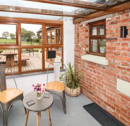 A sunroom with two metal chairs wooden seats a small round table with flowers a brick wall and a window at The Old Farm Shop in Narberth