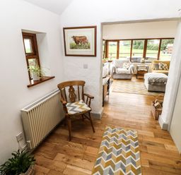 A hallway with a wooden chair and cushions and a view into a sitting room with armchairs and large windows at The Old Farm Shop in Narberth