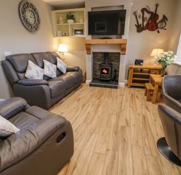 A living room with leather sofas a fireplace a wall-mounted TV a wooden floor and a small dining area at Lough Island Reavy Cottage in Kilcoo Mourne Mountains Newry County Down