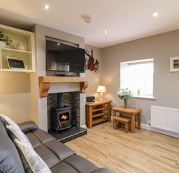 A living room with a leather sofa a wood burning stove under a mounted TV wooden furniture and a window at Lough Island Reavy Cottage in Kilcoo Mourne Mountains Newry County Down