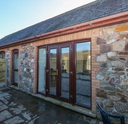 Stone exterior wall with wooden framed glass doors and windows on a paved outdoor area at The Old Well Bungalow - Ty Mawr Farm in Cardiff
