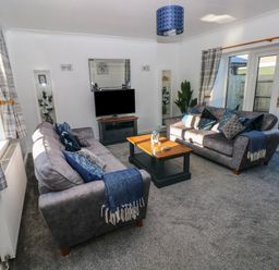 A living room with two grey sofas a wooden coffee table a television on a stand and glass doors at The Old Well Bungalow - Ty Mawr Farm in Cardiff