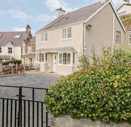 A two-story house with a gravel driveway and a black gate next to a bush and neighboring houses at Castell in Abersoch