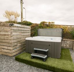 An outdoor hot tub with a cover and steps on artificial grass next to a wooden enclosure and plants at Castell Abersoch