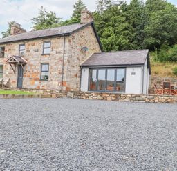 A stone cottage with a slate roof and gravel driveway with outdoor chairs and table at The Cottage in Llaniestyn
