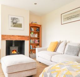 A living room with a beige sofa and ottoman a wood stove fireplace a wooden bookshelf and a television at The Cottage in Llaniestyn