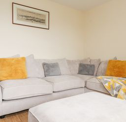 A corner sofa with yellow and gray cushions and a patterned throw with a framed picture on the wall at The Cottage in Llaniestyn