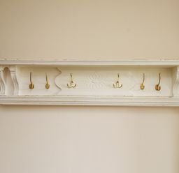 A wall mounted wooden coat rack with six gold hooks and decorative detailing at The Cottage in Llaniestyn