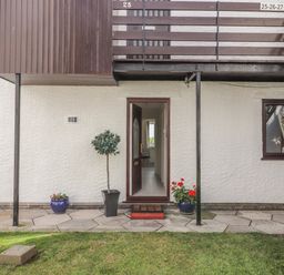 A ground floor entrance door with a doormat between two flower pots and a small tree in a pot outside a residential building at Sunset Sands in Deganwy