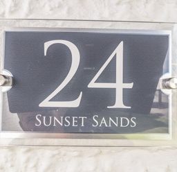 A house number sign with 24 and sunset sands on a textured wall at Sunset Sands in Deganwy