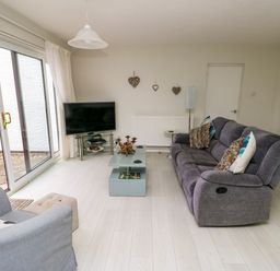 A living room with a gray sofa a blue armchair a glass coffee table a TV on a stand and sliding glass doors at Sunset Sands in Deganwy