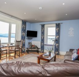 A living room with blue walls floral curtains wooden chairs a rocking horse a telescope and a brown leather sofa at Gadlys House - Waters Edge in Beaumaris