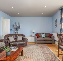 A living room with sofas a wooden coffee table a carpet a dining table and chairs at Gadlys House - Waters Edge in Beaumaris