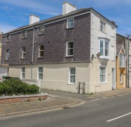 A street view of a three story building with a mix of brick and stucco walls and multiple windows in Beaumaris