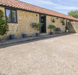 An exterior view of a stone building with a tiled roof and a small concrete patio with potted plants and a bench at Puddleducks Sherborne