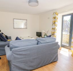 A living room with two grey sofas a floor lamp a small TV on a table and yellow patterned curtains at Puddleducks in Sherborne