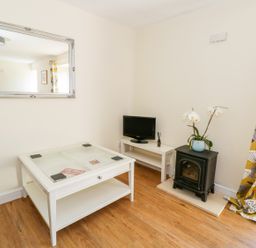 A living room with a glass top coffee table a small television a stove and yellow patterned curtains at Puddleducks in Sherborne