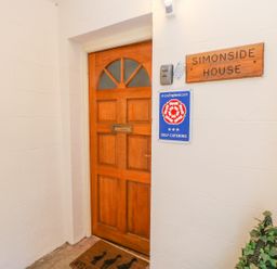 A wooden entrance door with a mail slot and a doormat a sign reading Simonside House and a self catering plaque on the wall at Simonside Apartment in Rothbury