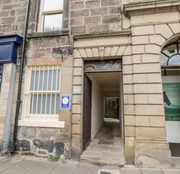 A narrow entrance passage between stone buildings with a window and an open door at Simonside Apartment in Rothbury