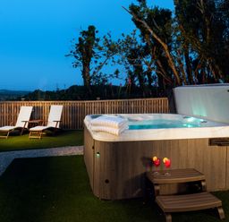 An outdoor area with a hot tub two lounge chairs and two drinks on a small table at Bear Cottage in Chacewater near Truro