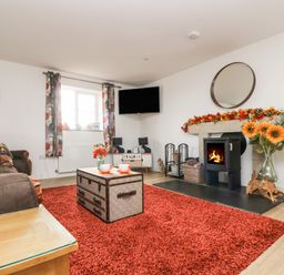 A living room with a fireplace and a red rug at Bear Cottage in Chacewater near Truro