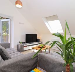 A living room with two grey sofas a wooden coffee table with fruit a television and an open door to a garden at The Crest in Helston