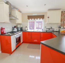 A kitchen with red lower cabinets beige upper cabinets and a window above the sink at Booster's Lodge in Stratford-upon-Avon