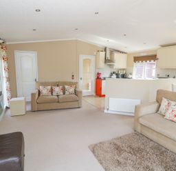 A living room with beige sofas and patterned cushions a wall-mounted TV and an open kitchen at Booster's Lodge in Stratford-upon-Avon
