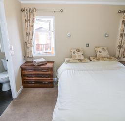 A bedroom with a double bed two windows bedside tables and an en suite bathroom at Boosters Lodge in Stratford-upon-Avon