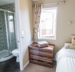 A bedroom with a bed next to a window and a chest of drawers beside an ensuite bathroom at Boosters Lodge in Stratford-upon-Avon