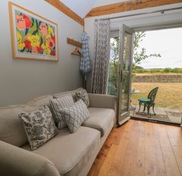 A living room with a sofa and open door leading to outdoor seating at The Lodge at Mortons in Hankerton