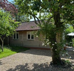 A cottage with trees and a patio area at The Lodge at Mortons in Hankerton