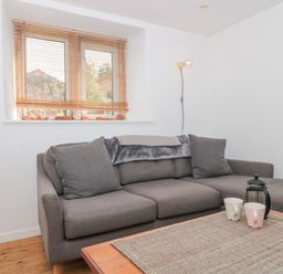 A gray sofa with cushions and a throw blanket beside a window with wooden blinds and a wooden coffee table with cups and a French press at Abbey Cottage Montacute
