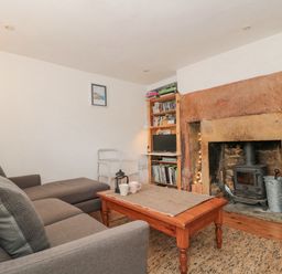 A living room with a gray sofa a wooden coffee table and a stone fireplace with a wood stove at Abbey Cottage Montacute