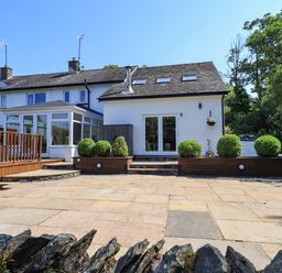 A backyard with paved patio area shrubs and a white house with glass doors and windows at Ellerbeck Bridge in Underbarrow near Kendal