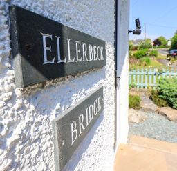 A close up of house name plaques on a wall with a garden and road in the background at Ellerbeck Bridge in Underbarrow near Kendal