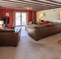 A living room with brown leather sofas a wood burning stove and a television at Ellerbeck Bridge in Underbarrow near Kendal