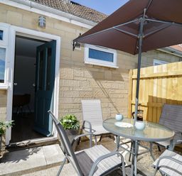 An outdoor patio with a glass table and four chairs under an umbrella at Troopers Cottage in Frome