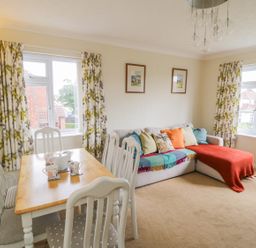 A living room with a dining table and chairs and a sofa with cushions at Sea-u-Soon in Runswick Bay