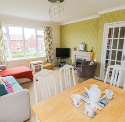 A living room with a sofa, armchair, small tables, TV, fireplace, dining table with teapot and cups at Sea-u-Soon in Runswick Bay