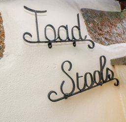Decorative black metal signs reading Toad and Stools on a white wall with stone accents at Toadstools in Rame Cross near Penryn