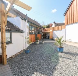 An outdoor courtyard with gravel ground and potted plants next to a white building with wooden accents at Toadstools in Rame Cross near Penryn
