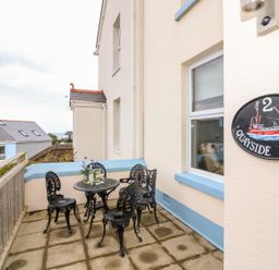 An outdoor patio with a black metal table and four chairs next to a cream building with blue trim at Quayside View in Brixham